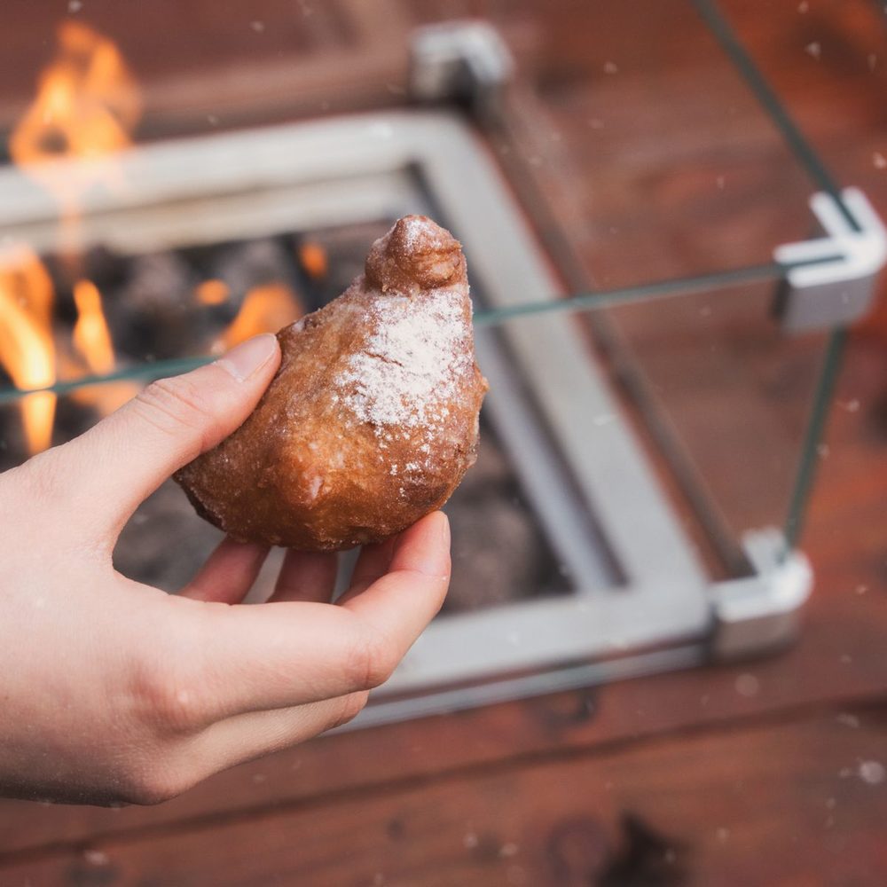 Een verse oliebol met poedersuiker in de hand